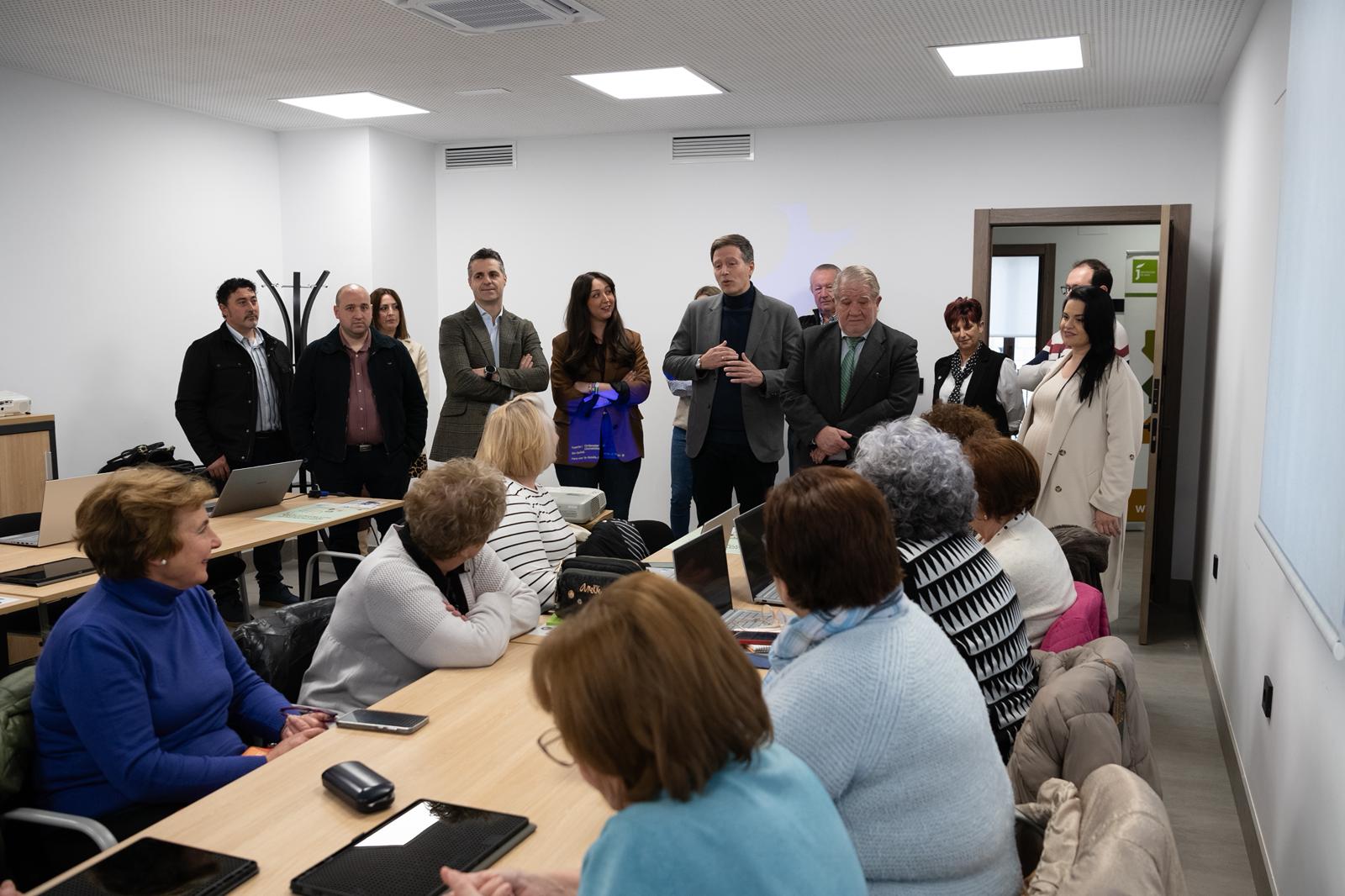 Participantes del programa de Capacitación Digital de la Diputación de Jaén trabajan con ordenadores portátiles y tablets en un aula informática, mientras responsables institucionales observan el desarrollo de la actividad.