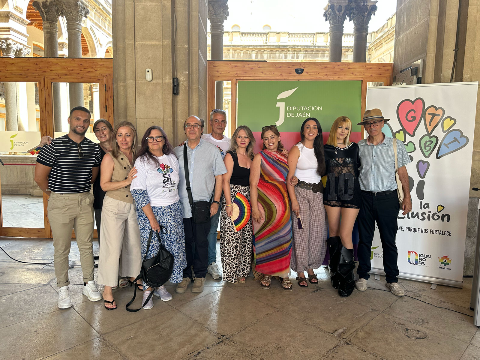 Grupo de asistentes y representantes institucionales posando juntos en la jornada por el Orgullo LGTBIQ+ de la Diputación de Jaén, junto a carteles a favor de la inclusión y la diversidad.